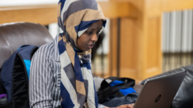 Student studying online for a business administration degree with a focus in Accounting, seated on a couch with a laptop.