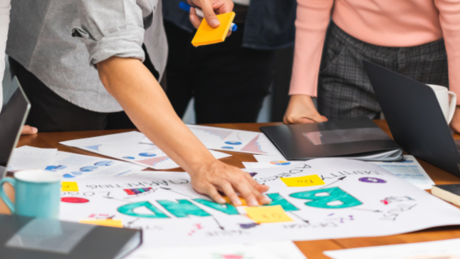 Students collaborating on a branding project as part of their business administration degree in Marketing, surrounded by charts, sticky notes, and laptops.