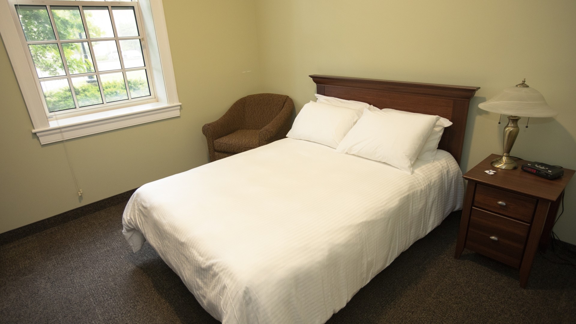 Governors Hall single suite with a double bed, bedside table and armchair. 