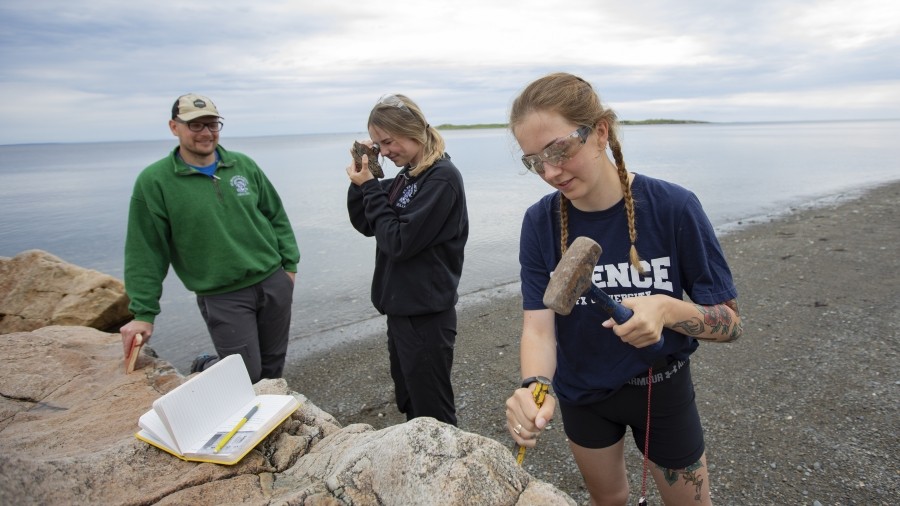 Earth Science students outdoors near the ocean examining rocks on a cloudy day.
