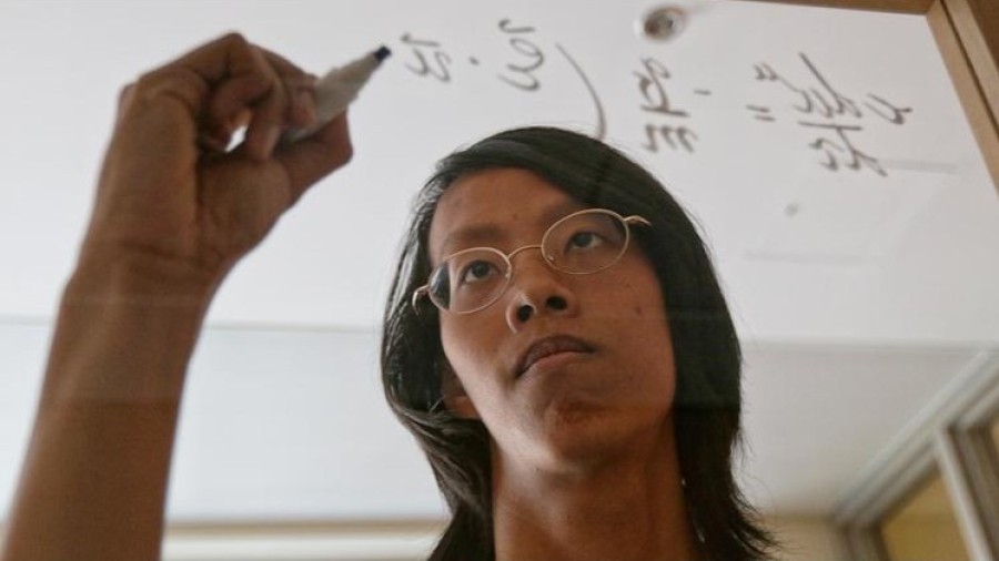 A student is writing math formula on the transparent glass board. 