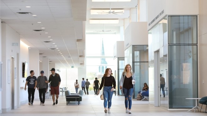 Students walking down a large, naturally lit corridor with light coloured walls