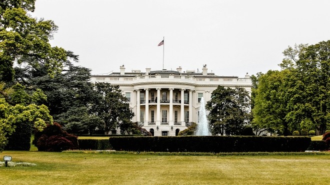 Photo of the White House, a multi-storey building with columns and an American flag on its roof. 