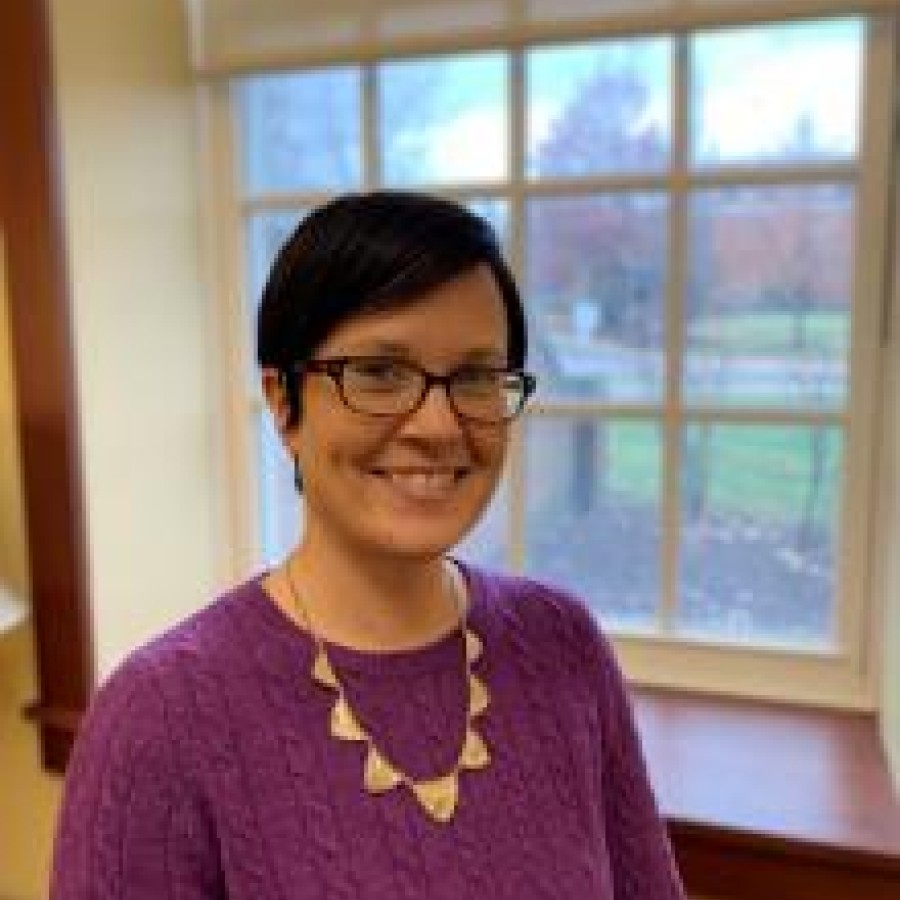 Headshot of Sarah McKenna smiling in purple sweater in front of a window. 