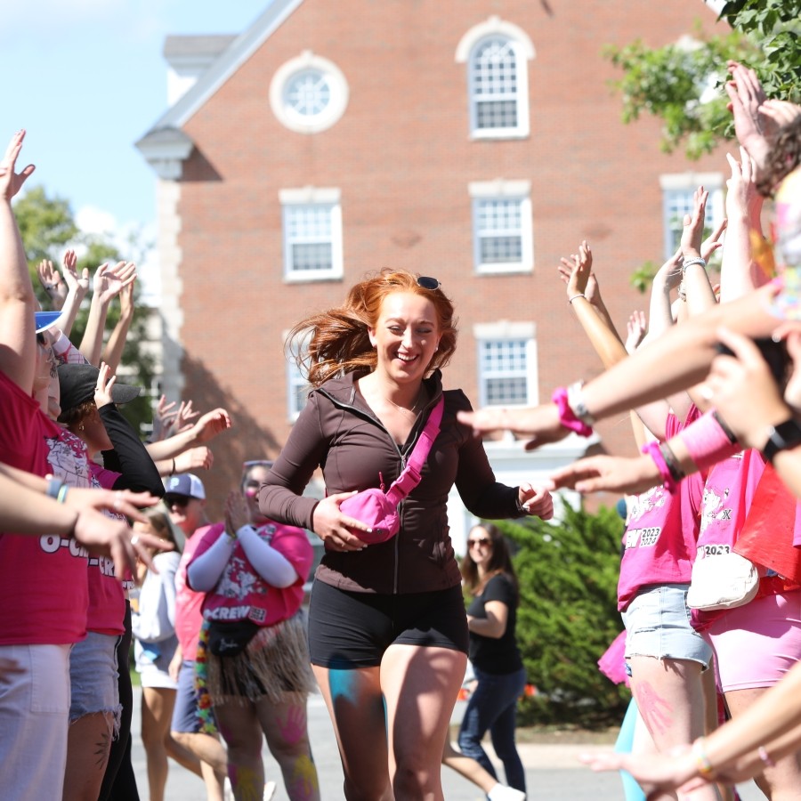 A happy student runs between two lines of cheering people in pink shirts