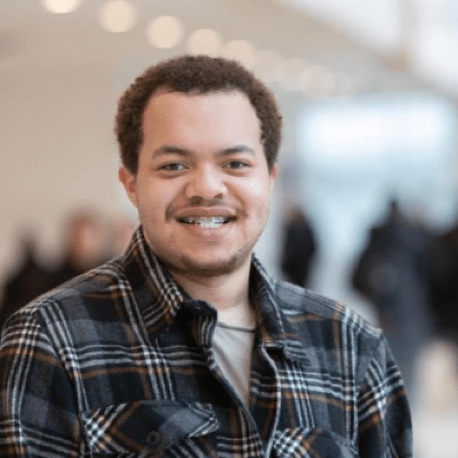 Headshot of a male student indoors with people walking in the background.