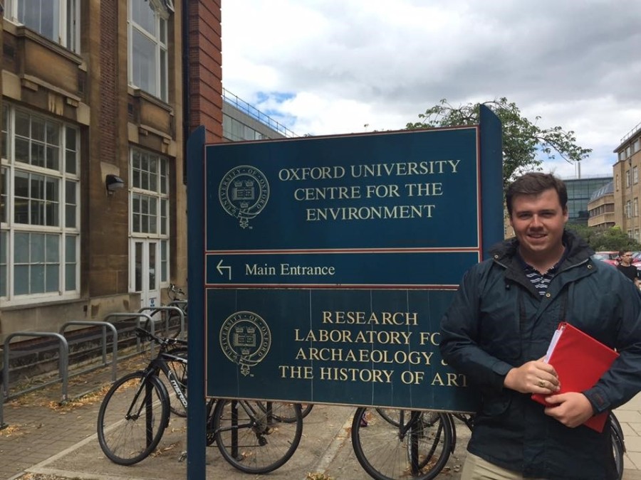 A person holding a book standing next to a sign and a building