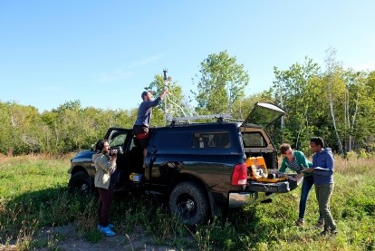 Three students unload equipment from a vehicle to conduct field research.