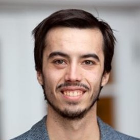 Headshot of Ben Lane-Smith smiling wearing black shirt and grey sports jacket. 