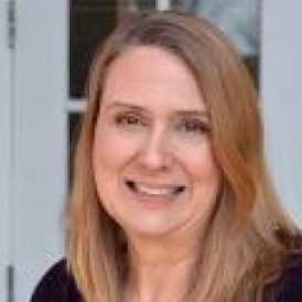 Headshot of Lindsey Arnold smiling in front of a white door. 