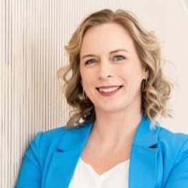 A woman in a blue jacket leaning against a wall
